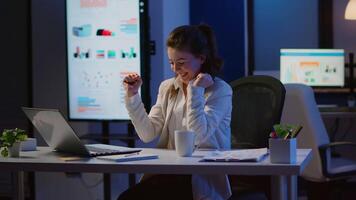 Excited woman feel ecstatic reading great online news on laptop working overtime in start up company office. Happy employee using modern technology network wireless studying writing, searching video