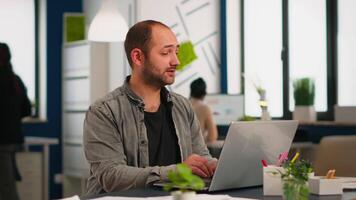 o negócio homem usando computador portátil digitando sentado às mesa dentro criativo acolhedor escritório concentrado em trabalho, enquanto diverso colegas trabalhando dentro fundo. moderno tecnologia, jovem pessoas e ocupação conceito. video