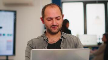 entusiasmado o negócio homem escrevendo uma relatório sentado às mesa dentro moderno comece o negócio escritório enviando mails digitando em computador portátil, cumprimento colega. homem trabalhando dentro financeiro companhia com diverso equipe. video