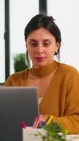 Cheerful business lady typing on laptop computer and smiling sitting at desk in busy start up office enjoying work in creative workplace. Diverse team analyzes statistics data in modern company video