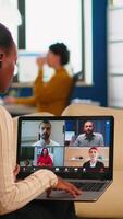 africano Gerente mulher discutindo com controlo remoto colegas usando ligar segurando computador portátil sentado em sofá dentro o negócio moderno escritório. diverso colegas de trabalho planejamento Novo financeiro projeto dentro moderno companhia video