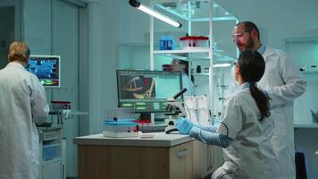 Team of biochemistry scientists developing drugs agains new virus, doctor checking samples while nurse taking noters on clipboard in modern equipped laboratory. Multiethnic scientists working video