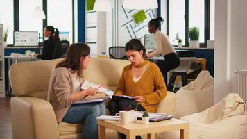 Stressed busineswomen arguing, yealing at each other during work hours sitting on the couch, while diverse colleagues working scared in background. Women throwing papers, conflicts at work concept video