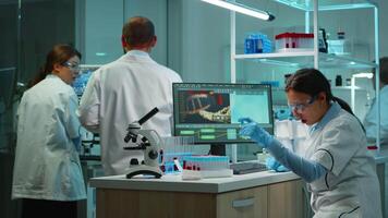 Scientist team checking virus development using high tech writing analysis results on computer in modern equipped lab at night. Doctors examining vaccine evolution with special tools for research. video