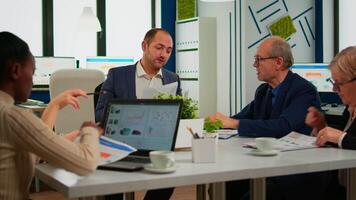 Businessman in suit talking to diverse business people partners sitting at conference table. Project leader discussing with teamworkers in meeting broadroom, group negotiations speaking with clients video