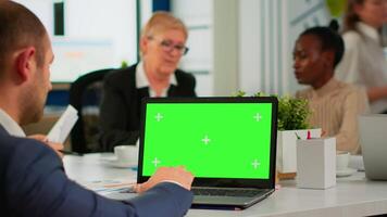 Back view of business man sitting conference desk using laptop with green screen talking with colleague while team working on background. Multiethnic coworkers planning project on chroma key display video
