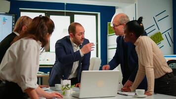 Diverse businesspeople working in teamwork discussing project strategy using laptop standing at conference table. Manager executive analysing financial data during business meeting in broadroom video