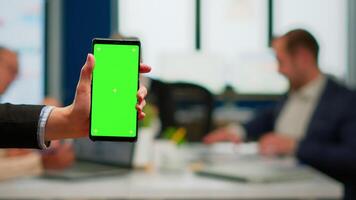 Businesswoman holding smartphone with green screen while diverse team working on background, businesspeople analysing financial statistics, Multiethnic coworkers planning project on chroma key display video