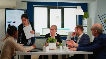 Secretary bringing coffee and meeting documents while smart multiethnic team planning new financial strategy during business conference. Manager briefing diverse teamworkers during brainstorming. video