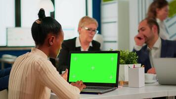 Over the sholder of african manager woman sitting at conference desk looking at laptop with green screen while diverse team working. Multiethnic people planning project on chroma key display video