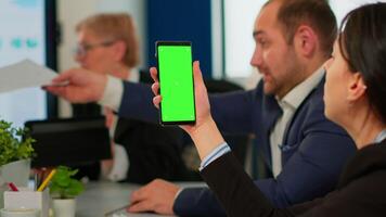 Businesspeople analysing annual financial reports sitting at desk while employee holding phone with green screen monitor. Leader explainig project strategy using greenscreen pc with chroma key display video