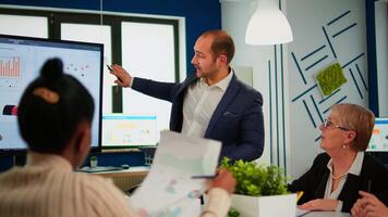 Comapany CEO holding clipboard and pointing on digital interactive whiteboard with growth analysis statistics and data. Diverse people working in broadroom during conference discussing startup problems video