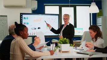 Chief analyst holding meeting presentation for a team of economists. Manager showing digital interactive whiteboard with growth analysis, charts, statistics, data, diverse people working in broadroom video