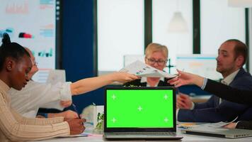 Group of business people discussing company plan with mockup laptop in front of camera, pc ready for financial project presentation placed on desk. Leader using green screen pc with chroma key display video