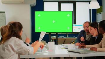 In corporate office meeting room stands green mock-up screen TV or interactive digital whiteboard in horizontal mode. Multiethnical businesspeople working, brainstorming in professional start up video