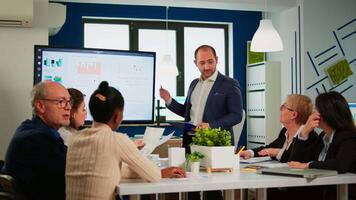 Manager pointing on digital interactive whiteboard with growth analysis, charts, statistics and data. Diverse people working in broadroom during conference meeting discussing company problems. video
