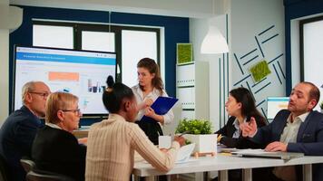 Diverse employees team with young woman leader working together in modern boardroom, manager executive pointing at digital interactive whiteboard, discussing project statistics, sharing ideas video