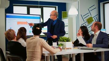 Team of analytics, economists businesspeople hold meeting presentation use shows digital interactive whiteboard with growth analysis, charts, statistics and data. People discussing in broadroom video