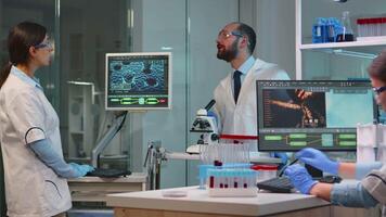 Man research scientist looking at samples under microscope while nurse writes informations on pc in modern equipped laboratory. Doctors working with various bacteria, tissue and blood tests video