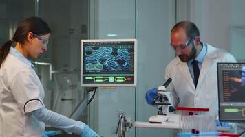 Scientist team checking virus development using microscope and nurse writing analysis results on computer overwork in modern equipped lab. Examining vaccine evolution using high tech for research. video