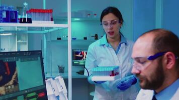 Chemist nurse holding test tubes bringing to doctor conducting DNA experiment discussing about medical treatment working overtime. Stuff examining virus evolution using high tech researching diagnosis video
