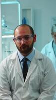 Vertical . Portrait of exhausted chemist looking at camera in modern equipped lab late at night. Team of biochemists examining virus evolution using high tech and chemistry tool for research, vaccine development video