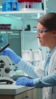 Vertical . Microbiologist working late at night for new vaccine in modern laboratory looking at samples under microscope. Coworkers examining virus evolution using high tech and chemistry tools for research. video