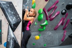 Determined girl climbing artificial wall at bouldering center photo