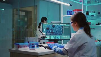 Chemist nurse sitting in scientific equipped lab examining virus evolution using high tech researching treatment against covid19 virus, typing results of tests on computer working overtime. video