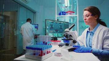 Team of scientist checking virus development using microscope analysing results at night in modern equipped lab. Group of chemists examining vaccine evolution using high tech for research. video