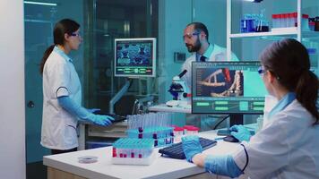 Scientist researcher using microscope in laboratory while nurse taking notes on computer working overtime. Medical healthcare technology and pharmaceutical research and development concept. video
