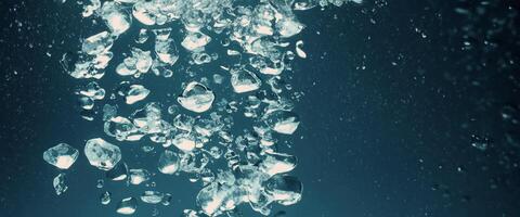 Water splashing and ice cube. Ice splashing into a glass of water. Underwater pouring ice cubes falling into clear watering background. Refreshing chill drinking. Ices in a glass with blue background photo