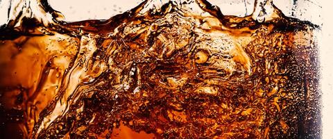 Splashing of Cola and Ice. Cola soda and ice splashing fizzing or floating up to top of surface. Close up of ice in cola water. Texture of carbonate drink with bubbles in glass. Cold drink background photo