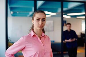 Portrait of young smiling business woman in creative open space coworking startup office. Successful businesswoman standing in office with copyspace. Coworkers working in background photo