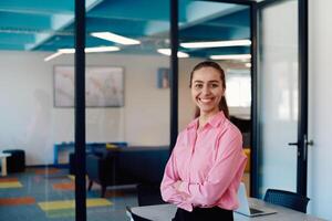 Portrait of a business woman in a creative open space coworking startup office with crossed arms. Successful businesswoman standing in office with copyspace. Associates work in the background photo