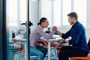In a modern startup office, a businessman and a businesswoman business colleagues engage in a symbolic arm-wrestling match, reflecting teamwork, competition, and innovation in their dynamic workplace. photo