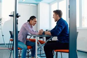 In a modern startup office, a businessman and a businesswoman business colleagues engage in a symbolic arm-wrestling match, reflecting teamwork, competition, and innovation in their dynamic workplace. photo