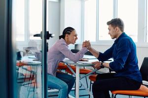 In a modern startup office, a businessman and a businesswoman business colleagues engage in a symbolic arm-wrestling match, reflecting teamwork, competition, and innovation in their dynamic workplace. photo