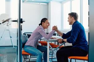 In a modern startup office, a businessman and a businesswoman business colleagues engage in a symbolic arm-wrestling match, reflecting teamwork, competition, and innovation in their dynamic workplace. photo
