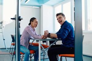 In a modern startup office, a businessman and a businesswoman business colleagues engage in a symbolic arm-wrestling match, reflecting teamwork, competition, and innovation in their dynamic workplace. photo