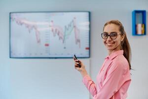 On Stage, Successful Female Speaker Presents Technological Product, Uses Remote Control for Presentation, Showing Infographics, Statistics Animation on Screen. Live Event Device Release photo