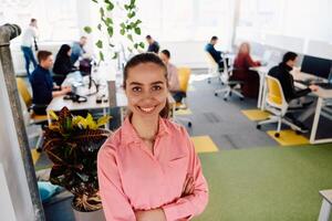 Portrait of young smiling business woman in creative open space coworking startup office. Successful businesswoman standing in office with copyspace. Coworkers working in background photo