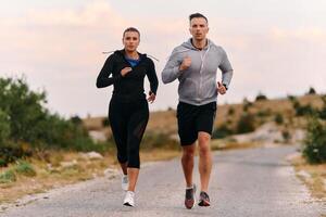 A couple dressed in sportswear runs along a scenic road during an early morning workout, enjoying the fresh air and maintaining a healthy lifestyle photo