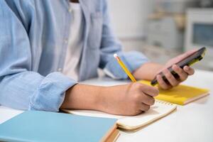 Teenage write in notebook and use mobile phone search data online to online learning university education. photo