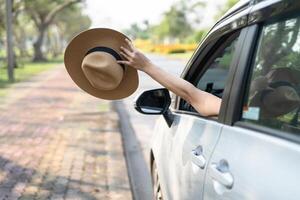 Happy enjoy and freedom in traveling trip with raised hand and holding hat outside of window car in summer vacation holiday. photo