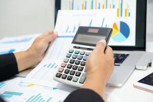 Asian accountant working and analyzing financial reports project accounting with chart graph and calculator in modern office, finance and business concept. photo