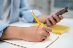 Teenage write in notebook and use mobile phone search data online to online learning university education. photo