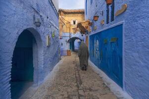 Man walking on narrow street in medina of blue city, Chefchaouen. Man wearing traditional clothes or Moroccan Djellaba, One of the most popular forms in Morocco. photo