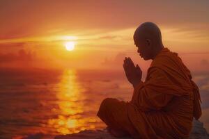 Thai Buddhist monk praying at sunrise while sitting on the seashore. photo