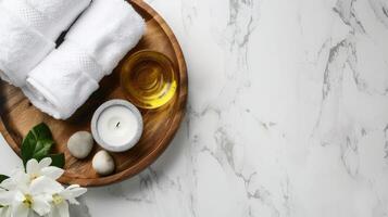 Massage set on a wooden round tray on a white marble table. View from above. White roll of towels, massage oil and candle. Background with copy space photo